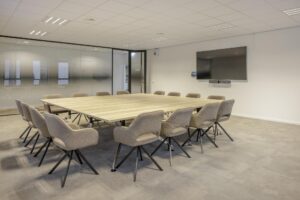 Modern conference room on Hiridostraat with a large wooden table, beige chairs, and a wall-mounted screen.